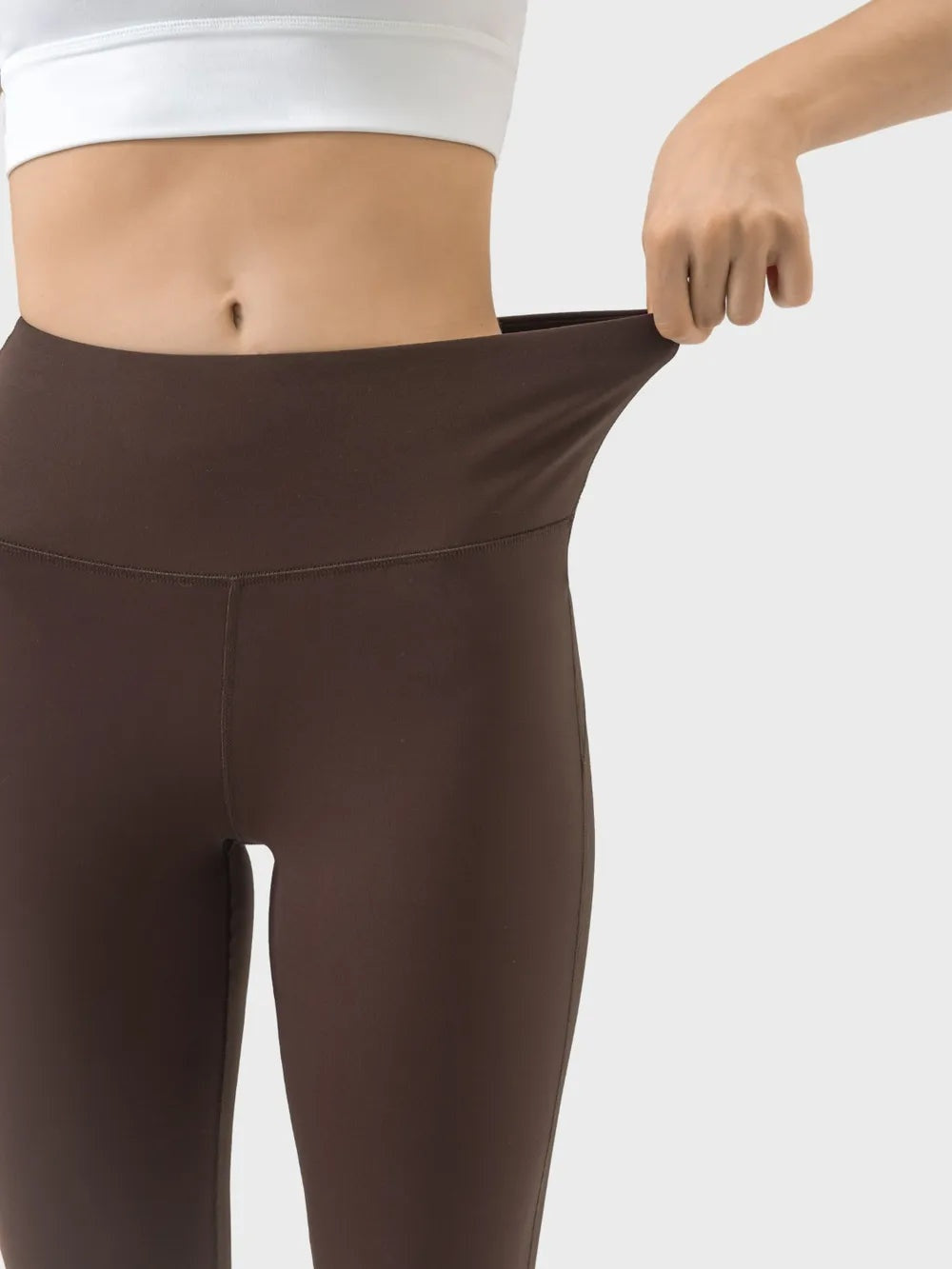 Close-up of a model wearing brown high-waist active pants with a fitted silhouette, stretch waistband, and visible front and hip seams.