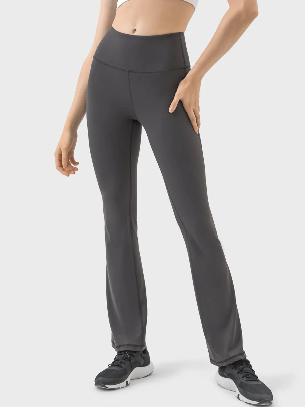 Model wears dark gray high-waist active pants with a wide waistband, sleek fitted silhouette, visible seam details, and slightly flared straight legs.