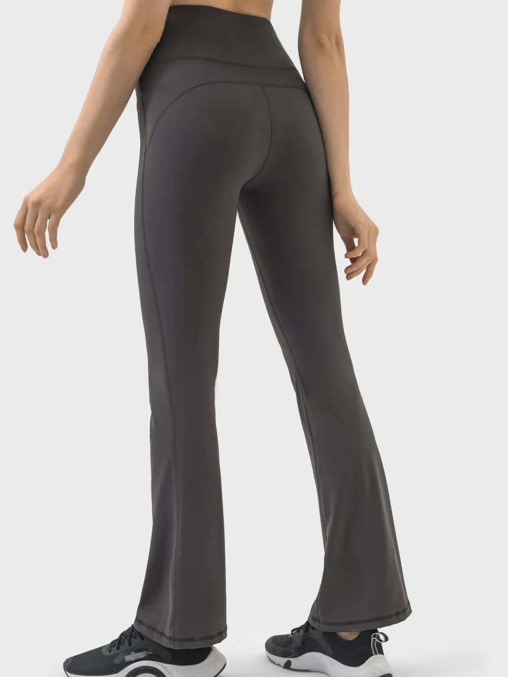 Model standing in dark gray high waist active pants with a smooth fitted silhouette, curved seam construction, and subtly flared legs.