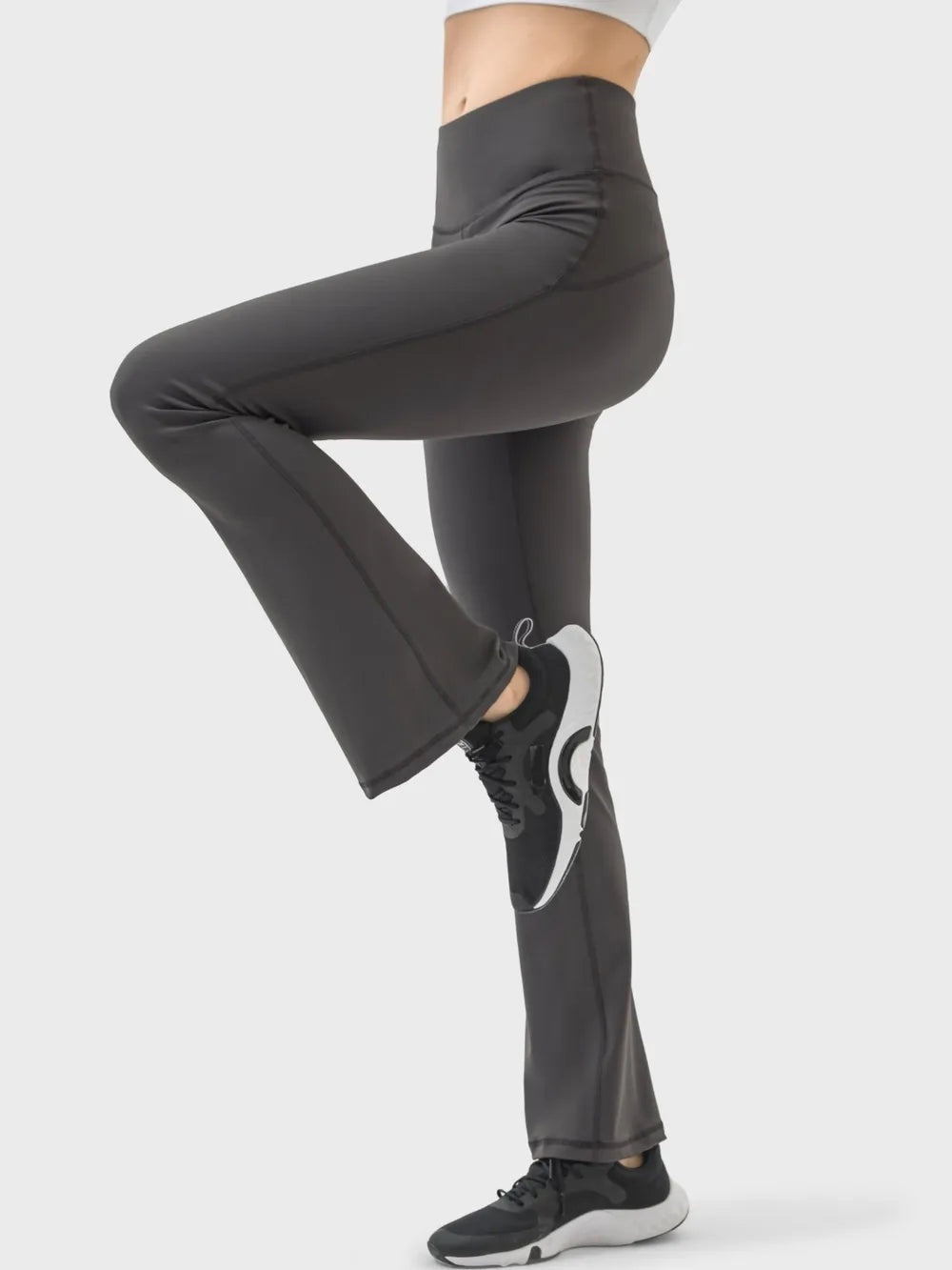 Model wearing black high-waist active pants with a sleek, stretchy straight-leg silhouette and visible construction seams, posed with one knee raised.