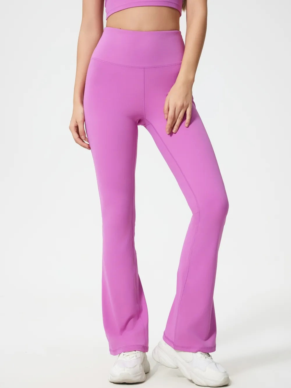 Model wearing bright pink high waist active pants with a smooth, stretchy fit, seamed construction, and flared legs, standing with one knee bent.