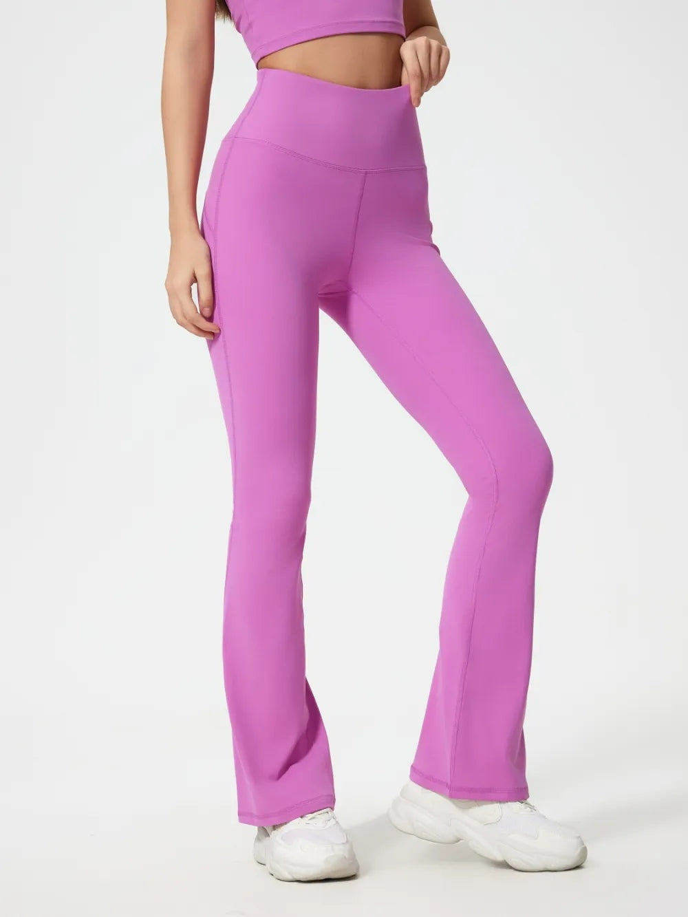 Model wears bright pink high-waist active pants with a fitted, stretchy silhouette, flared hems, and visible seam detailing while posing with one knee bent.