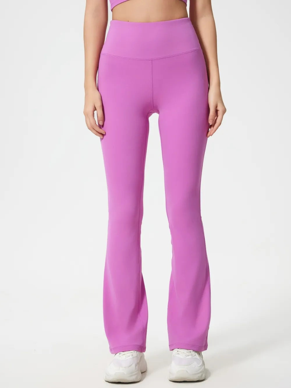 Model stands facing forward in bright pink high-waist active pants with a fitted stretch silhouette, curved waistband seam, and flared hems.