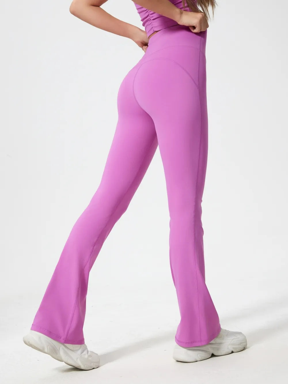 A model poses in bright pink high-waist active pants with a fitted silhouette, curved seam panels, and subtly flared legs.