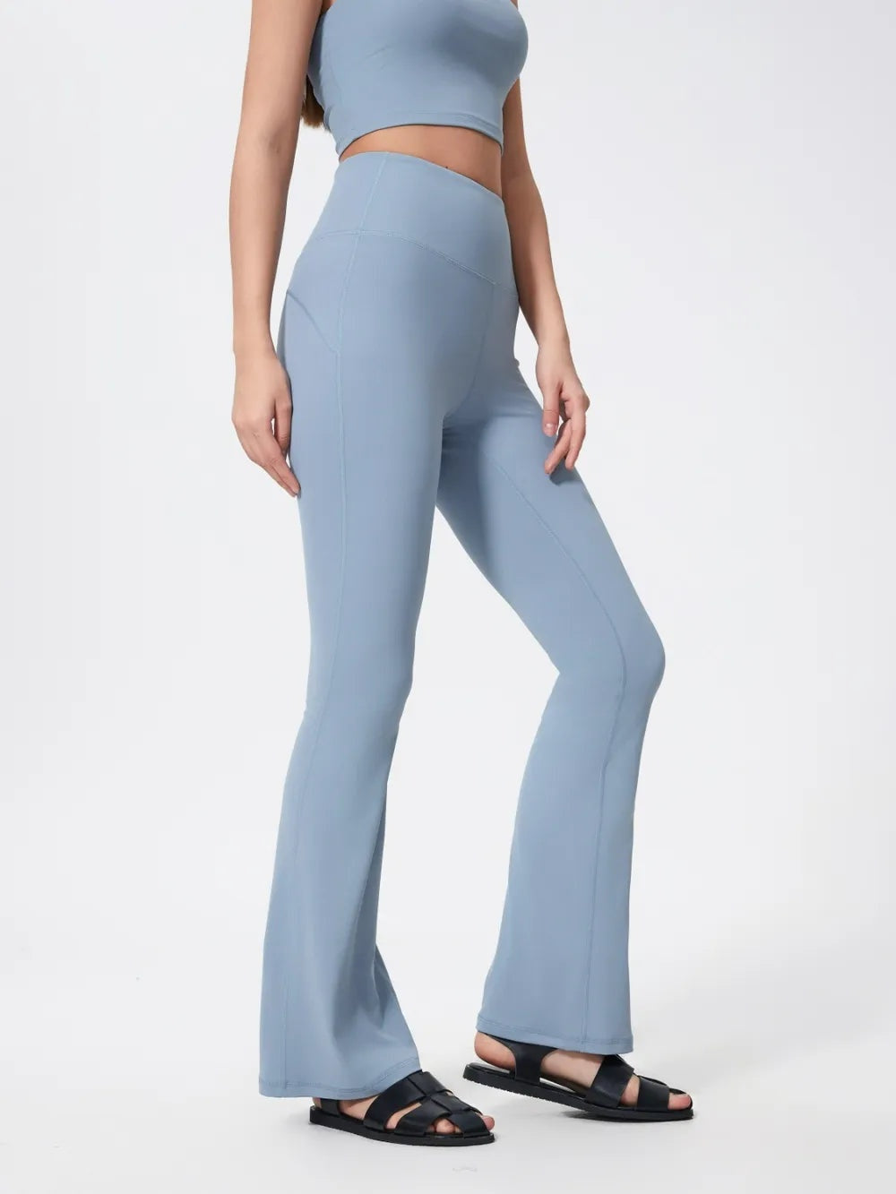 Model wearing light blue high-waist active pants with a close-fitting, highly stretchy silhouette, flared hems, and visible seam detailing, posed with one knee bent.