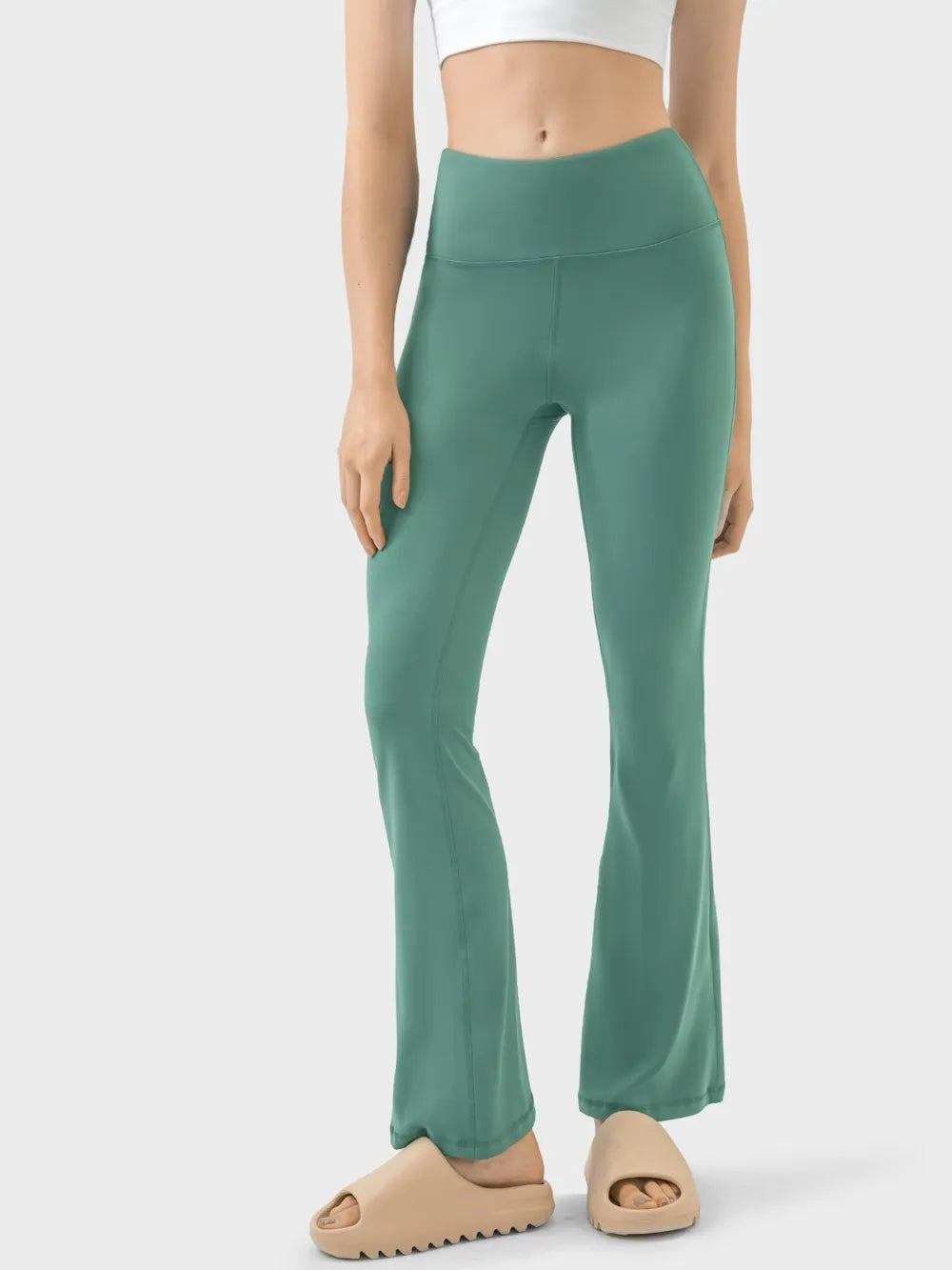 Model wearing green high-waist active pants with a smooth waistband, fitted stretch silhouette, and subtle front leg seams.