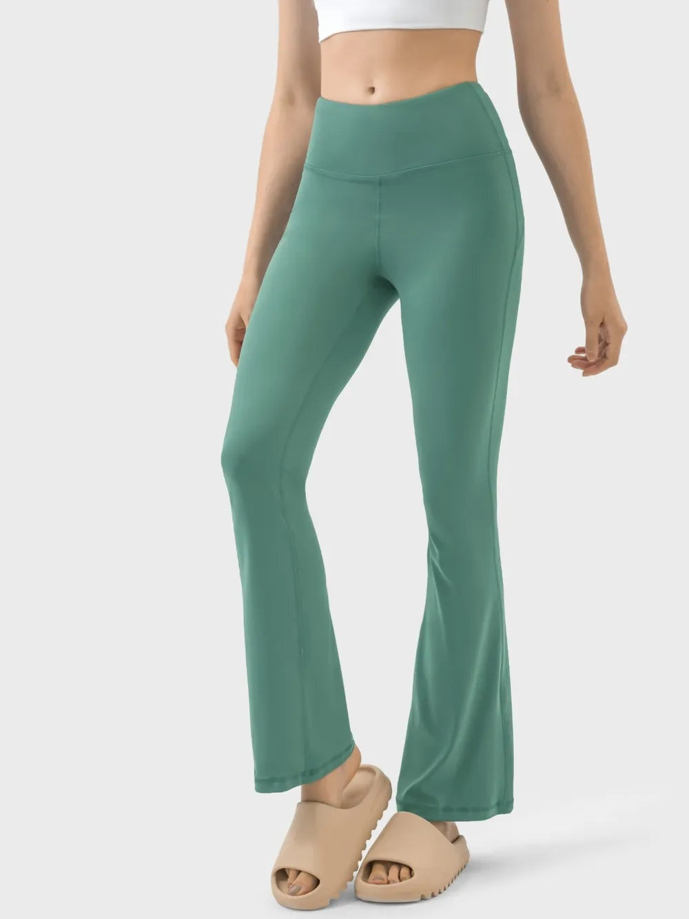 A model wears sage green high waist active pants with a wide waistband, fitted stretch silhouette, visible seam construction, and gently flared hems.