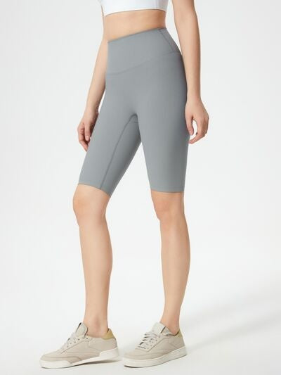 A model stands in gray high waist active shorts with a fitted, knee-length silhouette, smooth construction, and flexible stretch fabric.