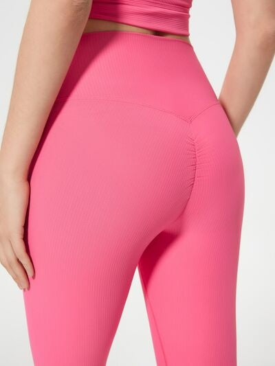 A model poses from behind in bright pink high-waist active shorts with a close, stretchy fit and curved seam construction.