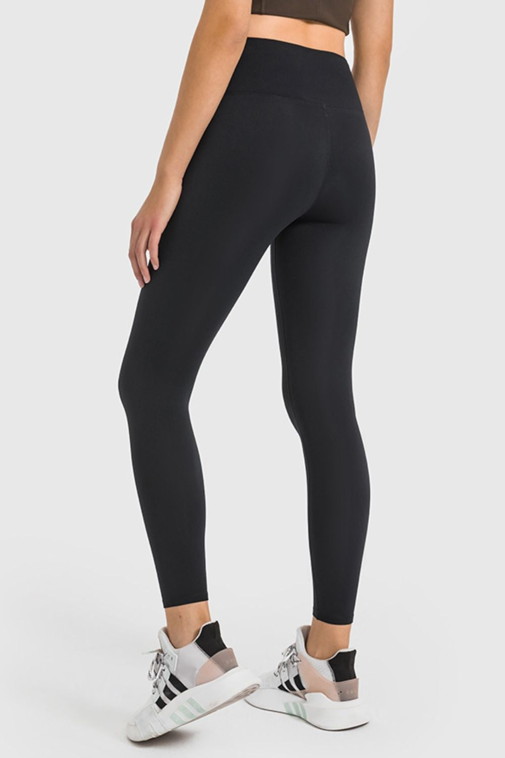 Model wearing black high-waist ankle-length yoga leggings with a smooth, close-fitting silhouette, shown from the back in a relaxed pose.