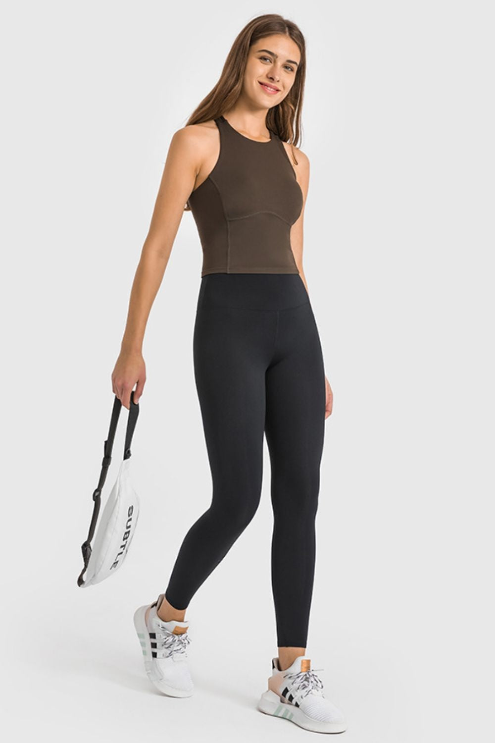 Model wearing black high-waist ankle-length yoga leggings with a smooth, stretchy fitted silhouette and wide waistband, standing with one leg crossed.