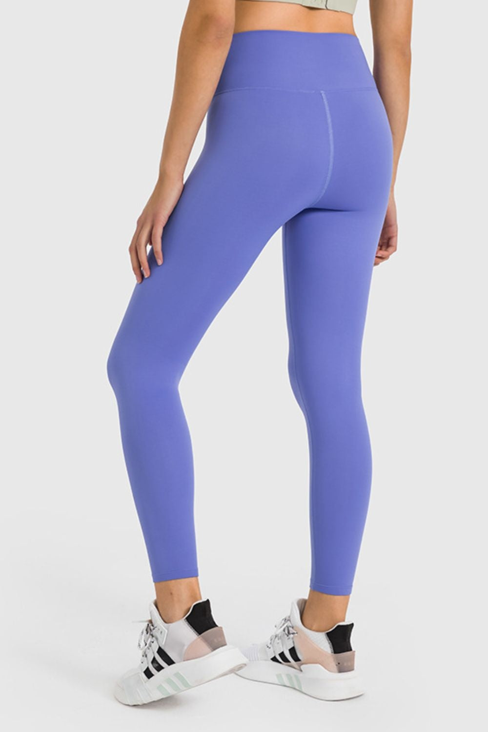 Model shown from behind wearing purple high-waist ankle-length yoga leggings with a smooth, stretchy close-fitting silhouette and visible center-back seam.