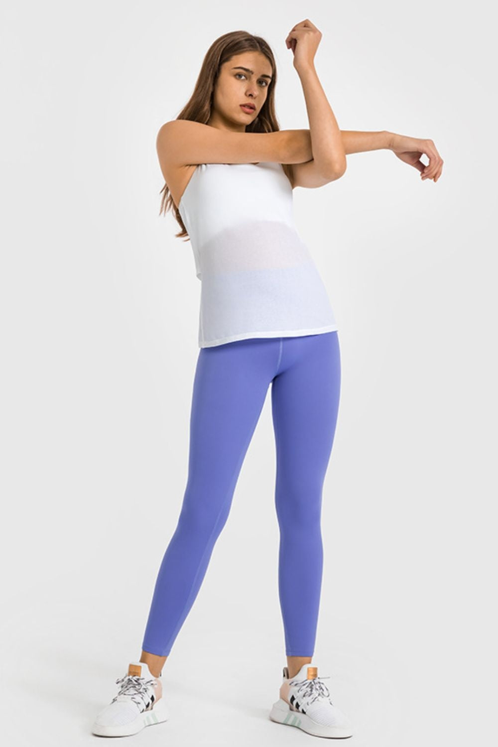 Model stretches in bright blue high-waist ankle-length yoga leggings with a smooth, stretchy fitted silhouette and clean ankle hems.