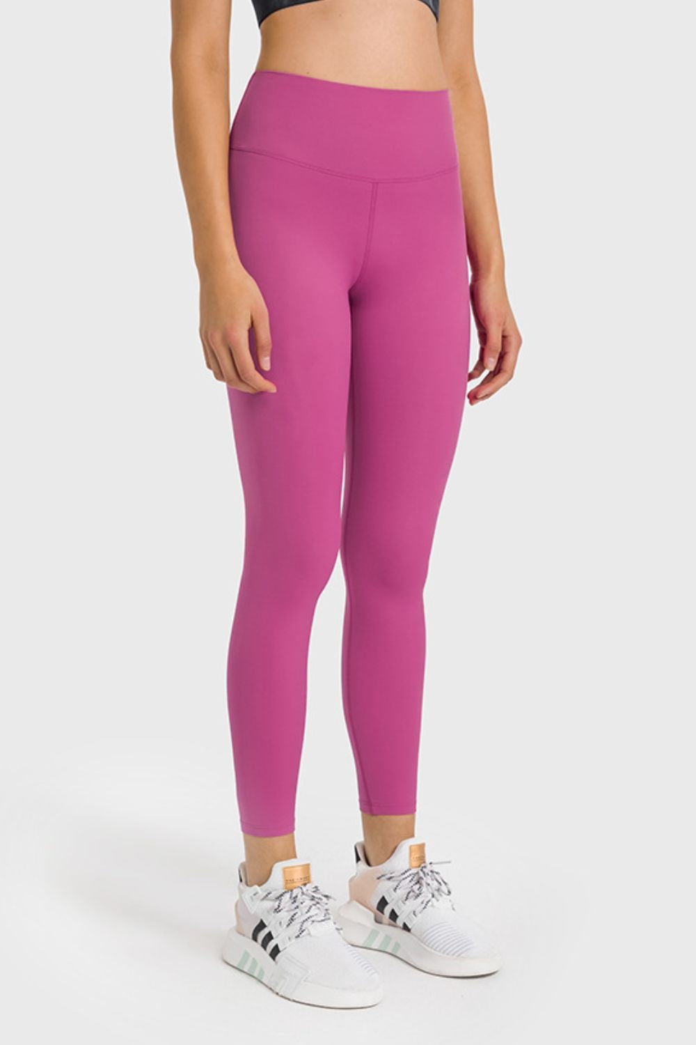 Model stands in bright pink high-waist ankle-length yoga leggings with a close-fitting silhouette, wide waistband, and visible front seam construction.