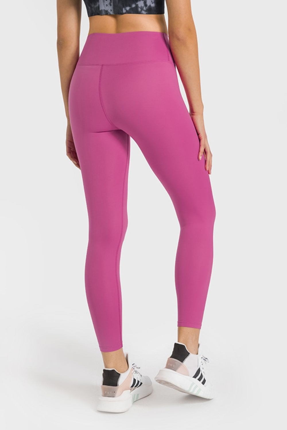 Model shown from behind wearing high-waist ankle-length yoga leggings in vibrant pink with a smooth, fitted silhouette and stretch construction.