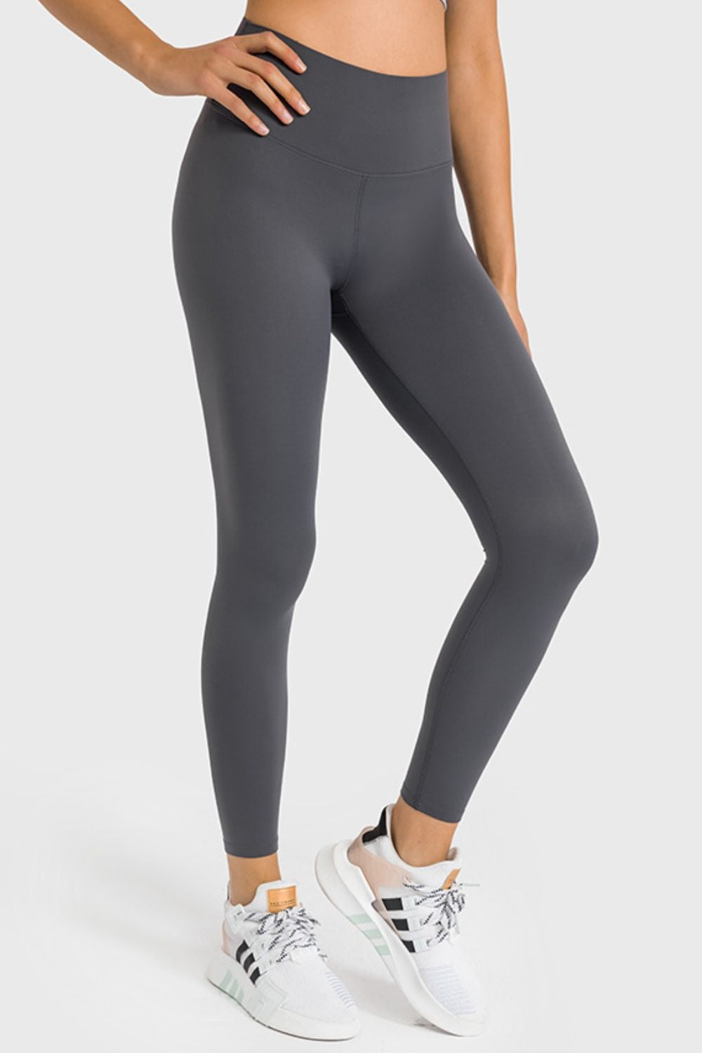 Model wearing dark gray high-waist ankle-length yoga leggings with a smooth, fitted silhouette, visible seams, and one hand resting on her hip.