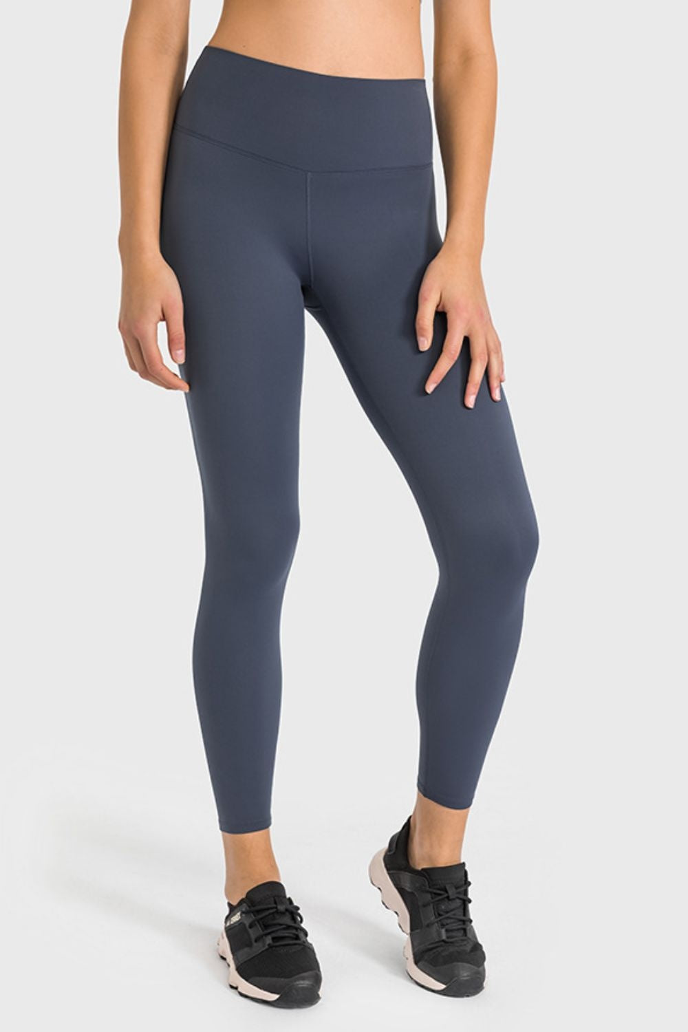 Model wearing dark navy high-waist ankle-length yoga leggings with a wide waistband, sleek fitted silhouette, and hands resting on her thighs.