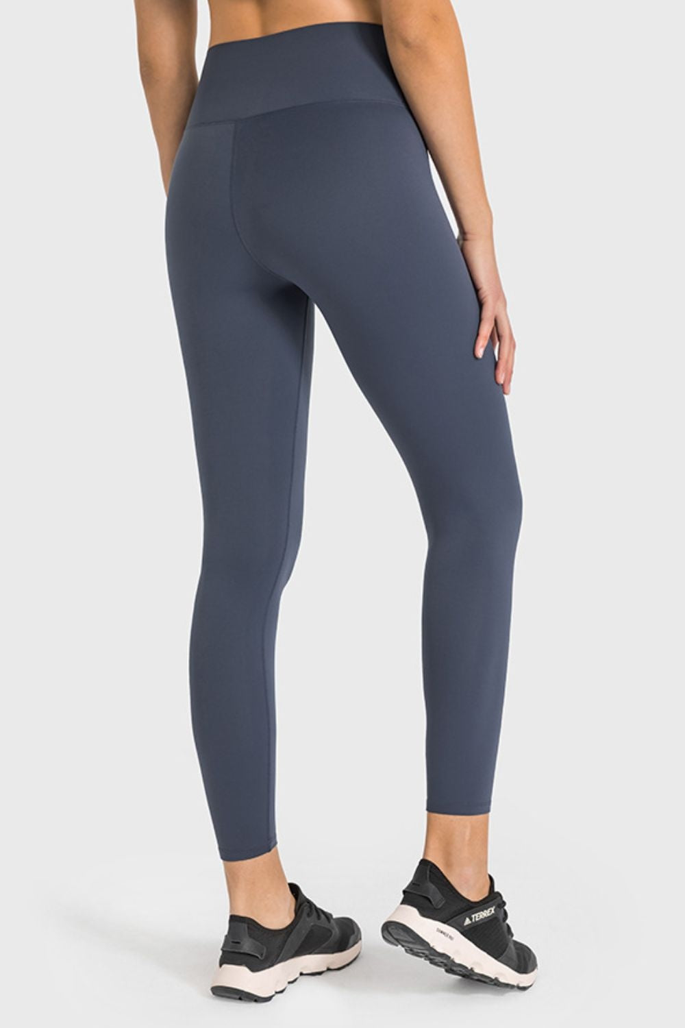 Model shown from behind in dark blue-gray high-waist ankle-length yoga leggings with a smooth, close-fitting silhouette and curved back seam.