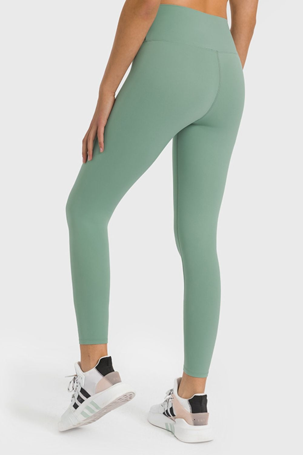 Model poses in sage green high-waist ankle-length yoga leggings with a smooth fitted silhouette, wide waistband, and visible rear seam construction.
