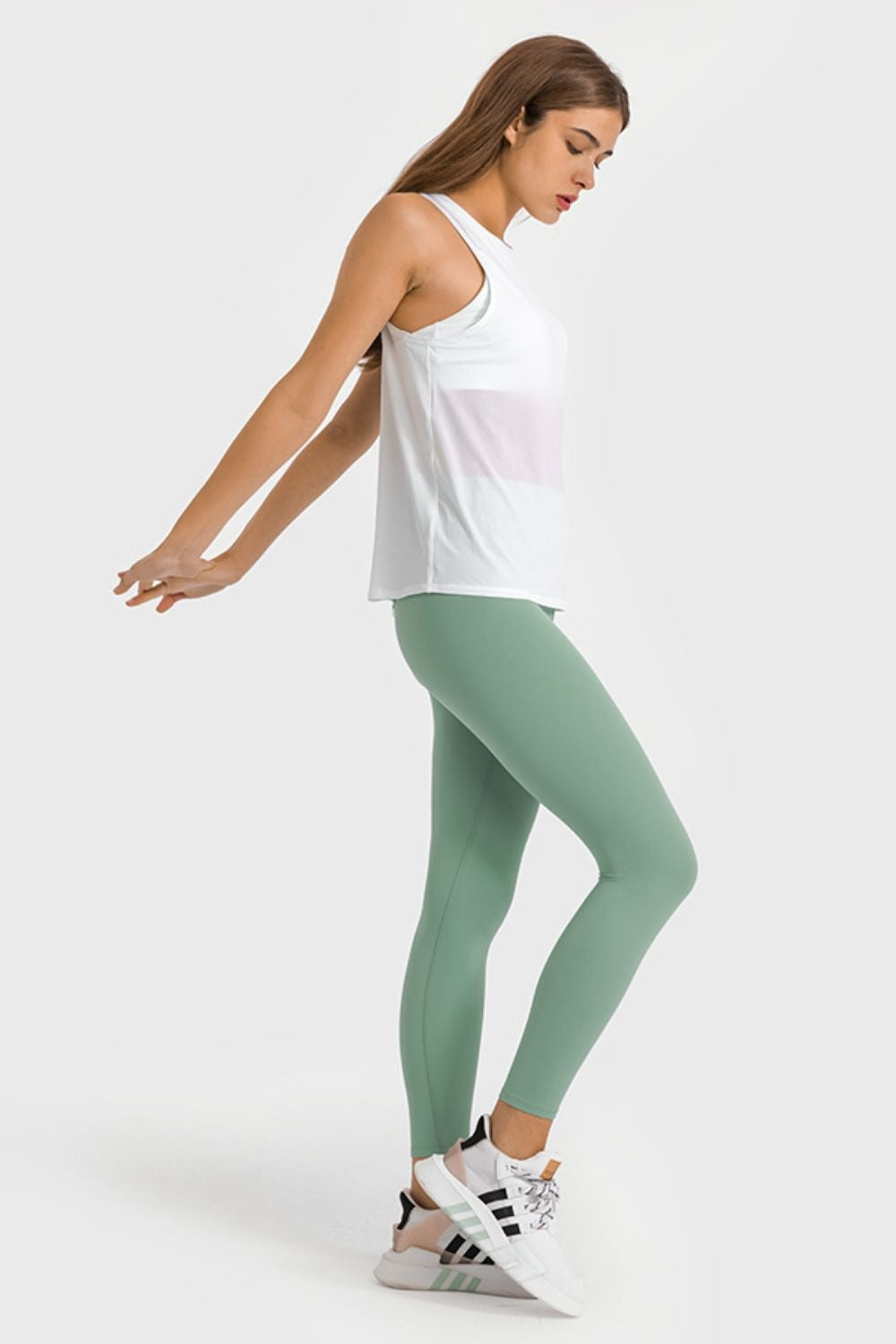 Model poses in ankle-length, high-waist yoga leggings with a smooth, close-fitting silhouette in sage green and visible stretch construction.