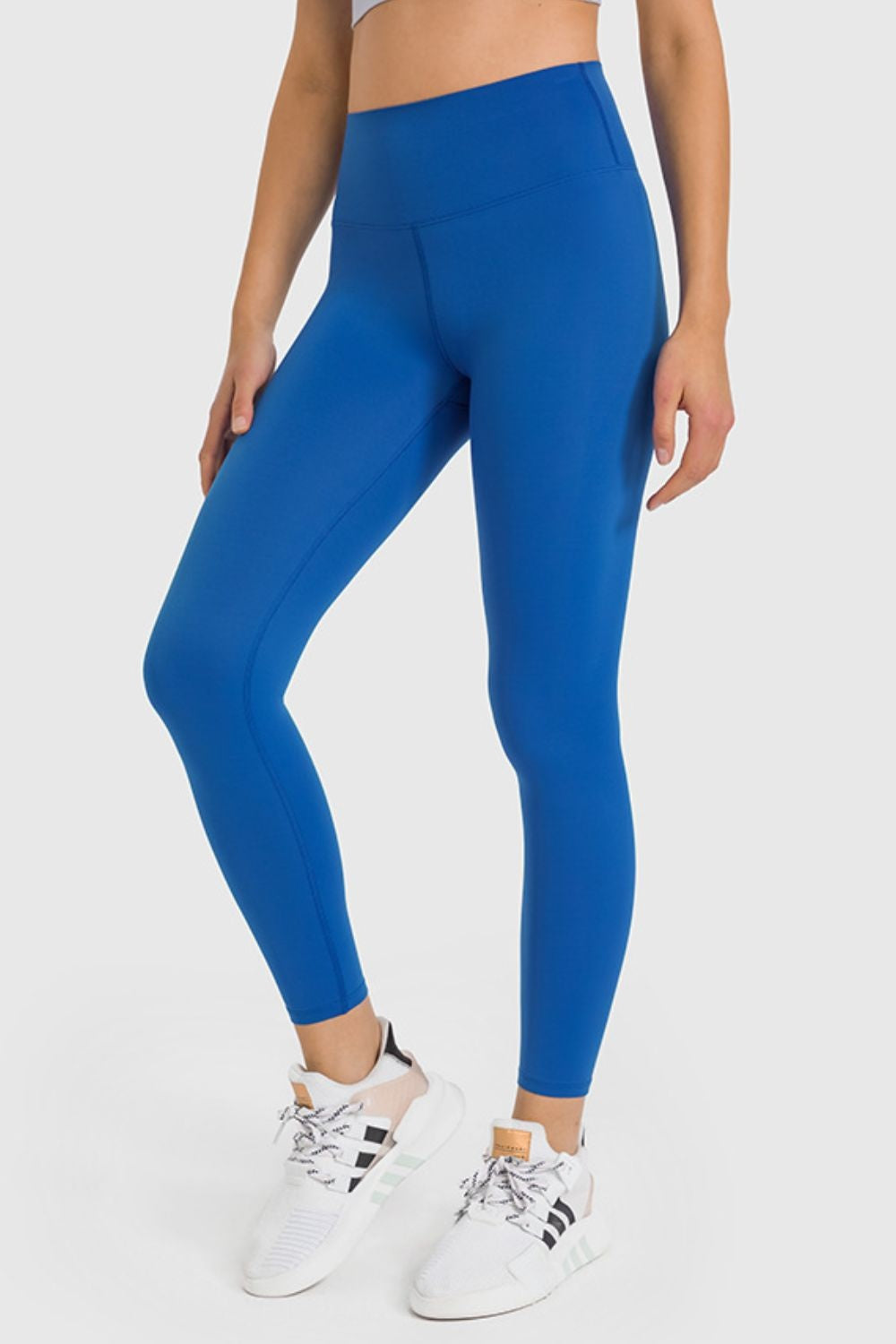 Model wears bright blue high-waist ankle-length yoga leggings with a smooth, stretchy close-fit silhouette and visible seam construction.