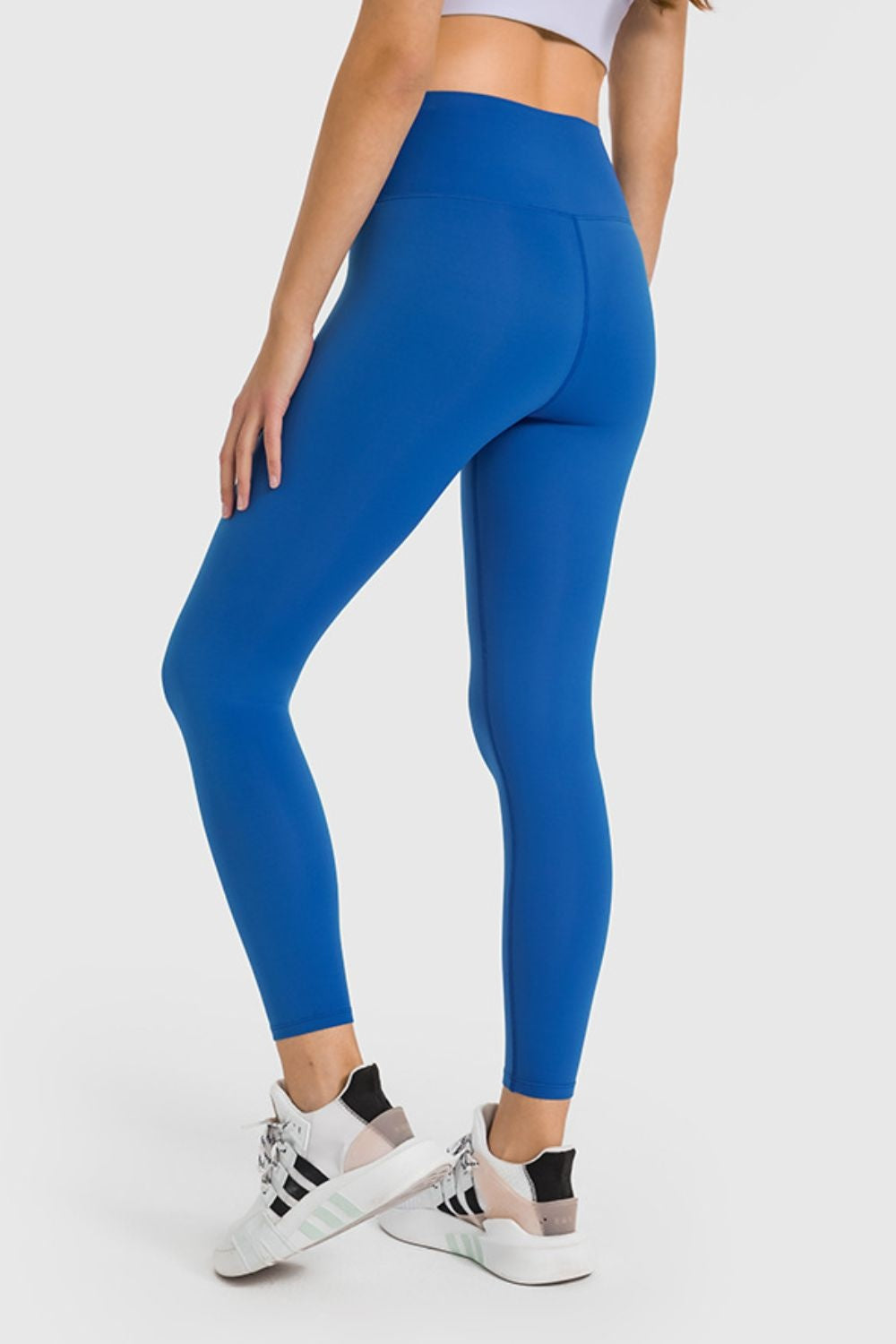 Model poses with one hand on her thigh, wearing bright blue high-waist ankle-length yoga leggings with a smooth, stretchy fitted silhouette and seamed construction.
