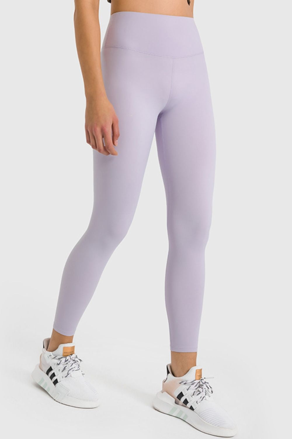 Model wearing lavender high-waist ankle-length yoga leggings with a smooth, fitted silhouette, flat seam construction, and one leg extended forward.