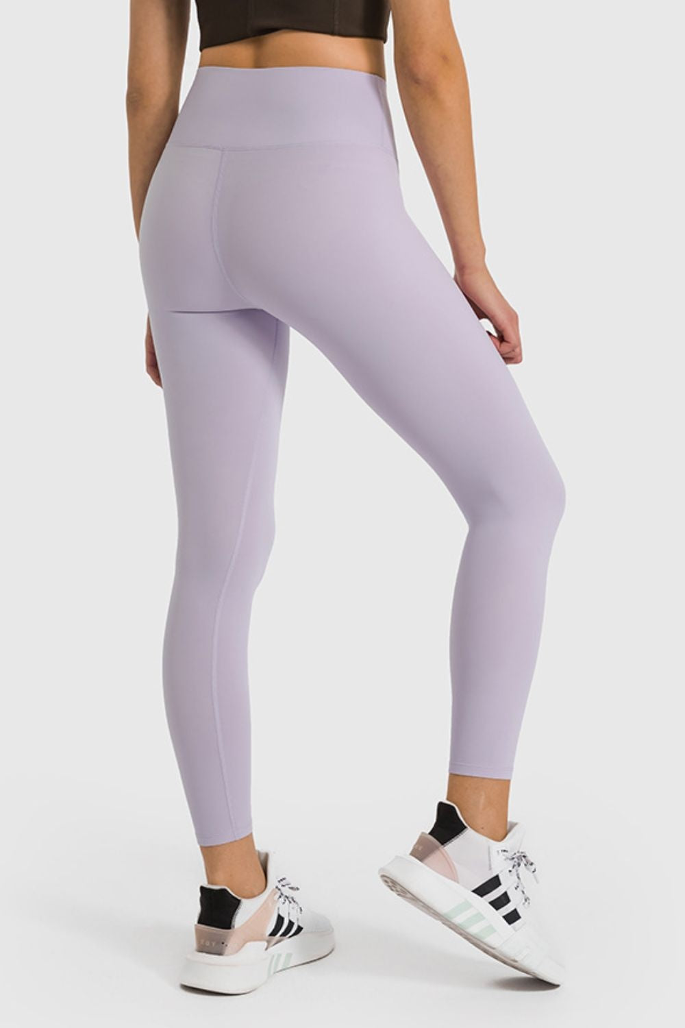 Model poses in lavender high-waist ankle-length yoga leggings with a smooth fitted silhouette, wide waistband, and visible curved back seam.