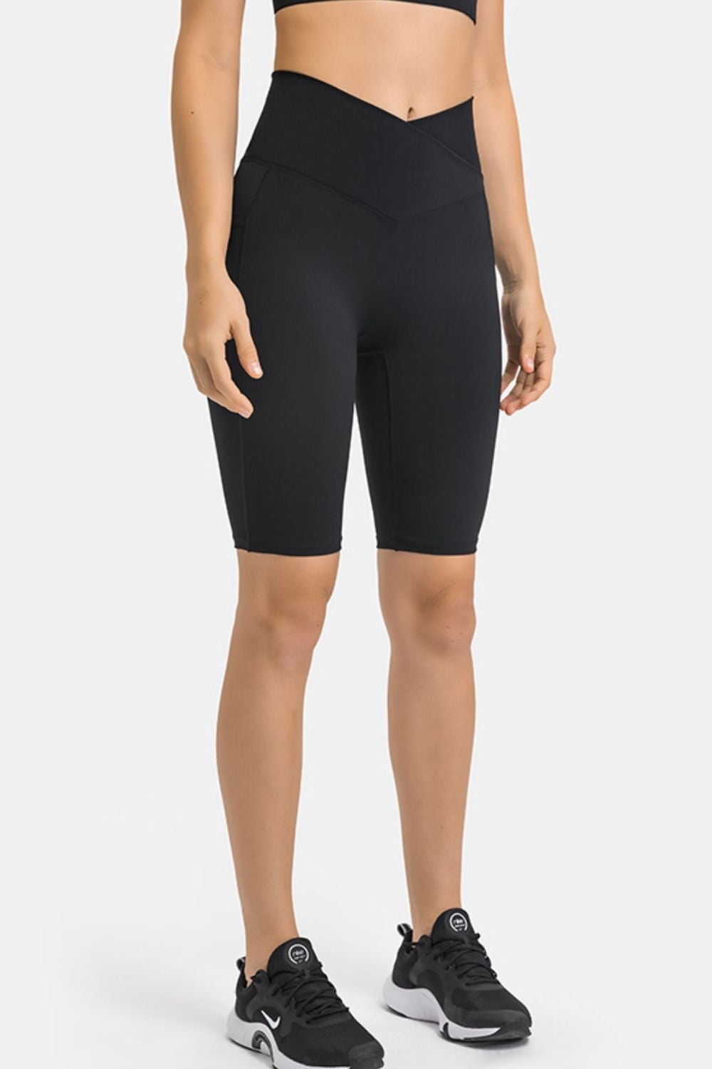 Model stands facing forward in black high-waist biker shorts with a smooth fitted silhouette, V-shaped waistband, and visible side pockets.