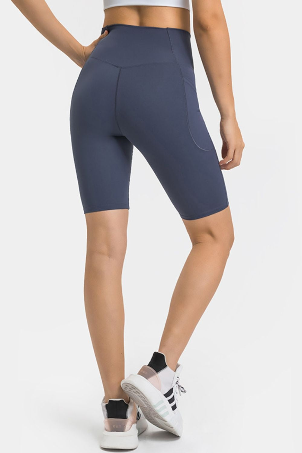 A model poses in navy high-waist biker shorts with a fitted knee-length silhouette, curved side pockets, and visible panel seams.