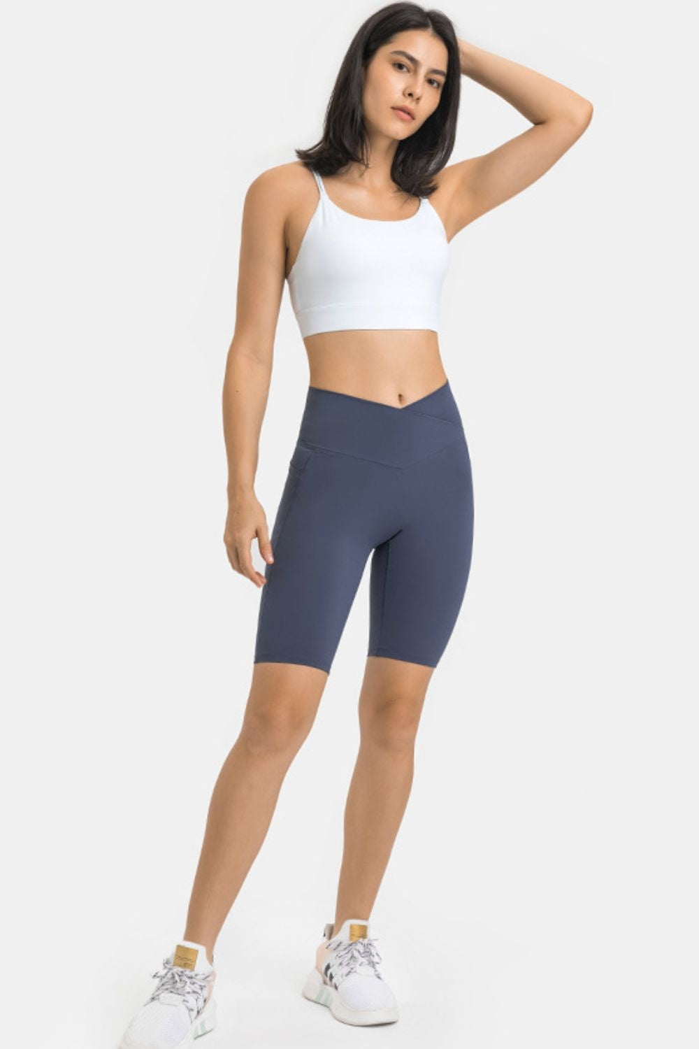A model poses in dark blue high-waist biker shorts with pockets, featuring a wide V-shaped waistband, fitted stretch silhouette, and knee-length hems.