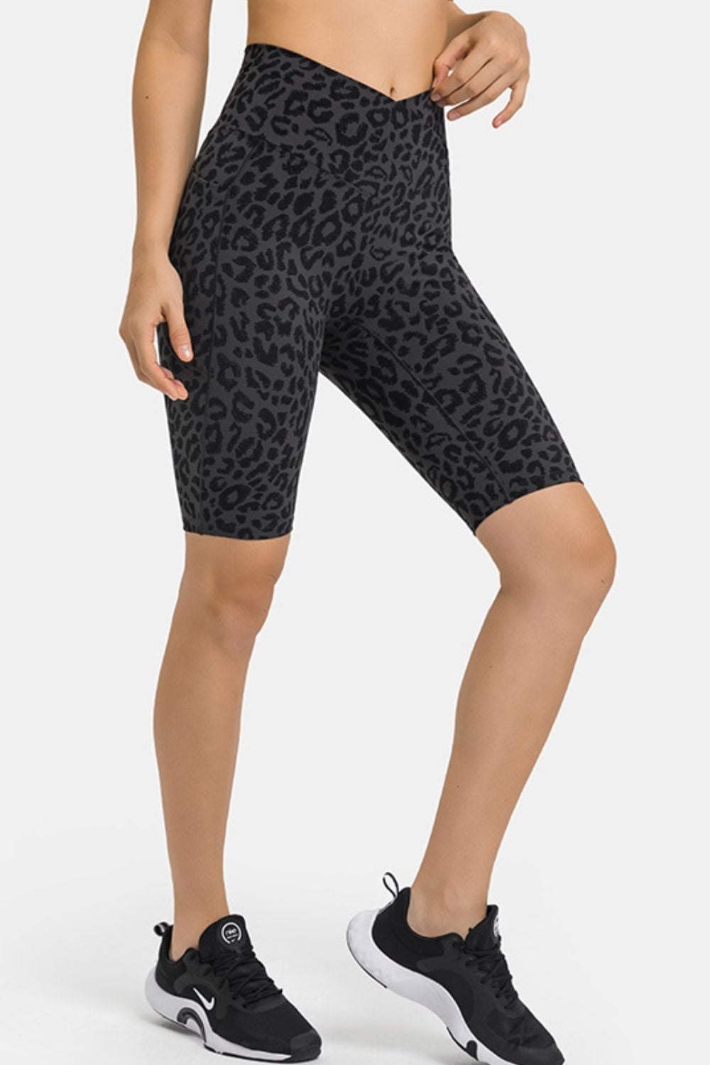 Model wears high-waist dark gray leopard-print biker shorts with a close, knee-length silhouette, stretch construction, and side pockets, posing with one hand at the waistband.