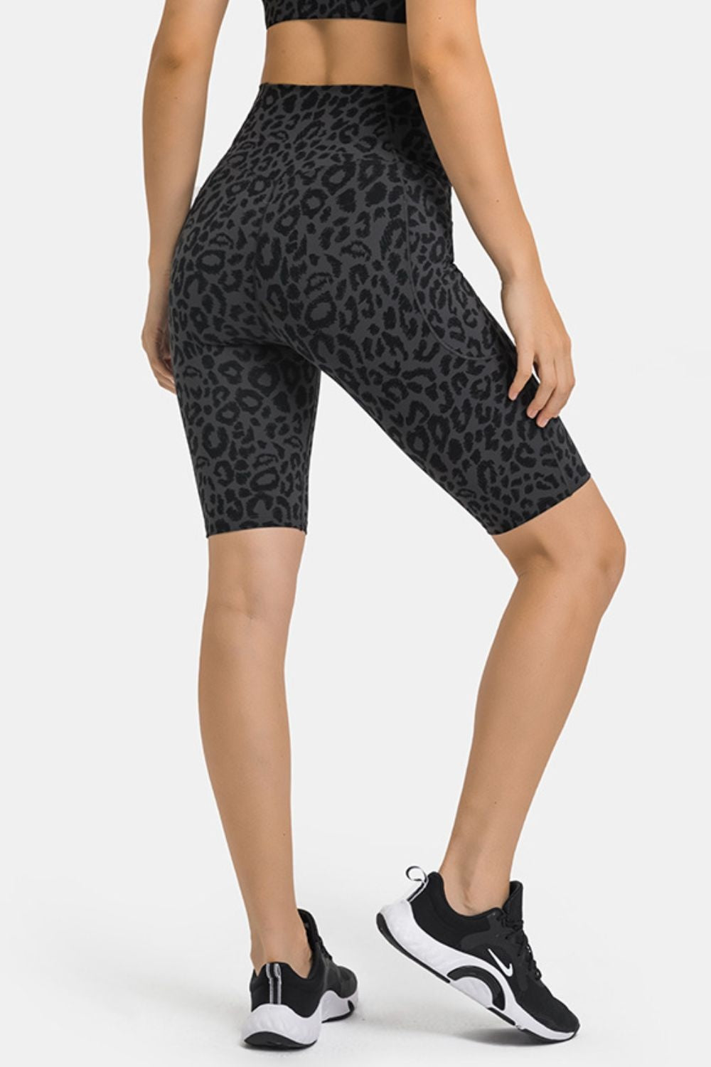 A model poses in high-waist black leopard-print biker shorts with a fitted knee-length silhouette and visible side pockets.