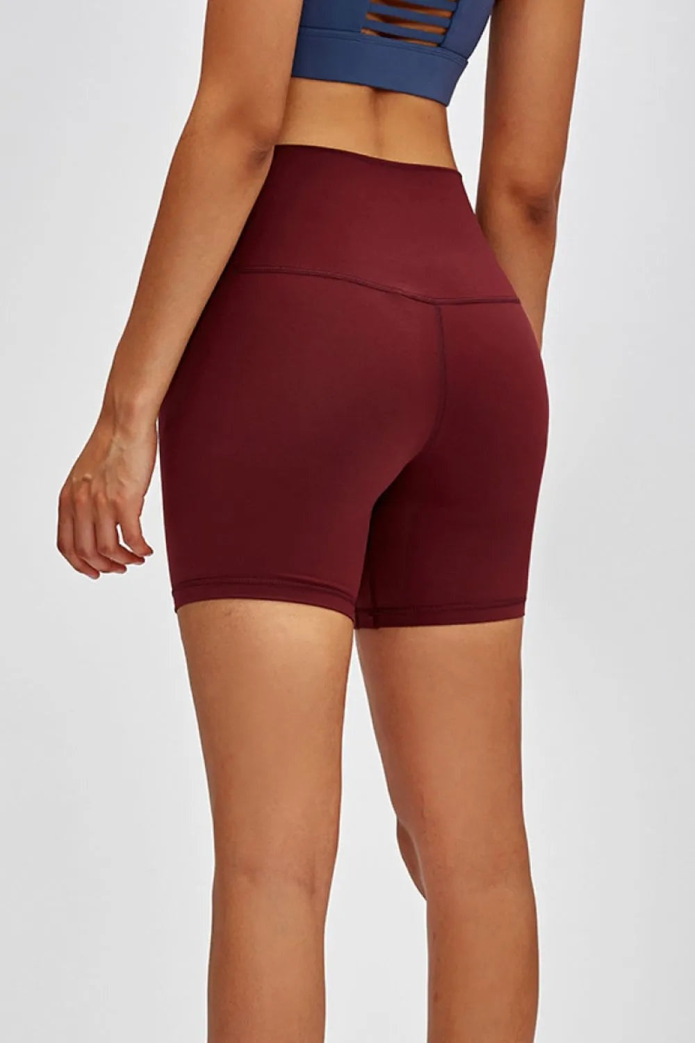 Back view of a model wearing burgundy high waist training shorts with a fitted, stretchy biker-length silhouette and visible center-back seams.
