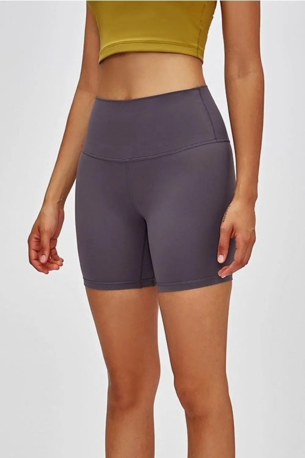 Model wearing dark gray high-waist training shorts with a stretchy fitted silhouette, wide waistband, curved seam, and mid-thigh length.