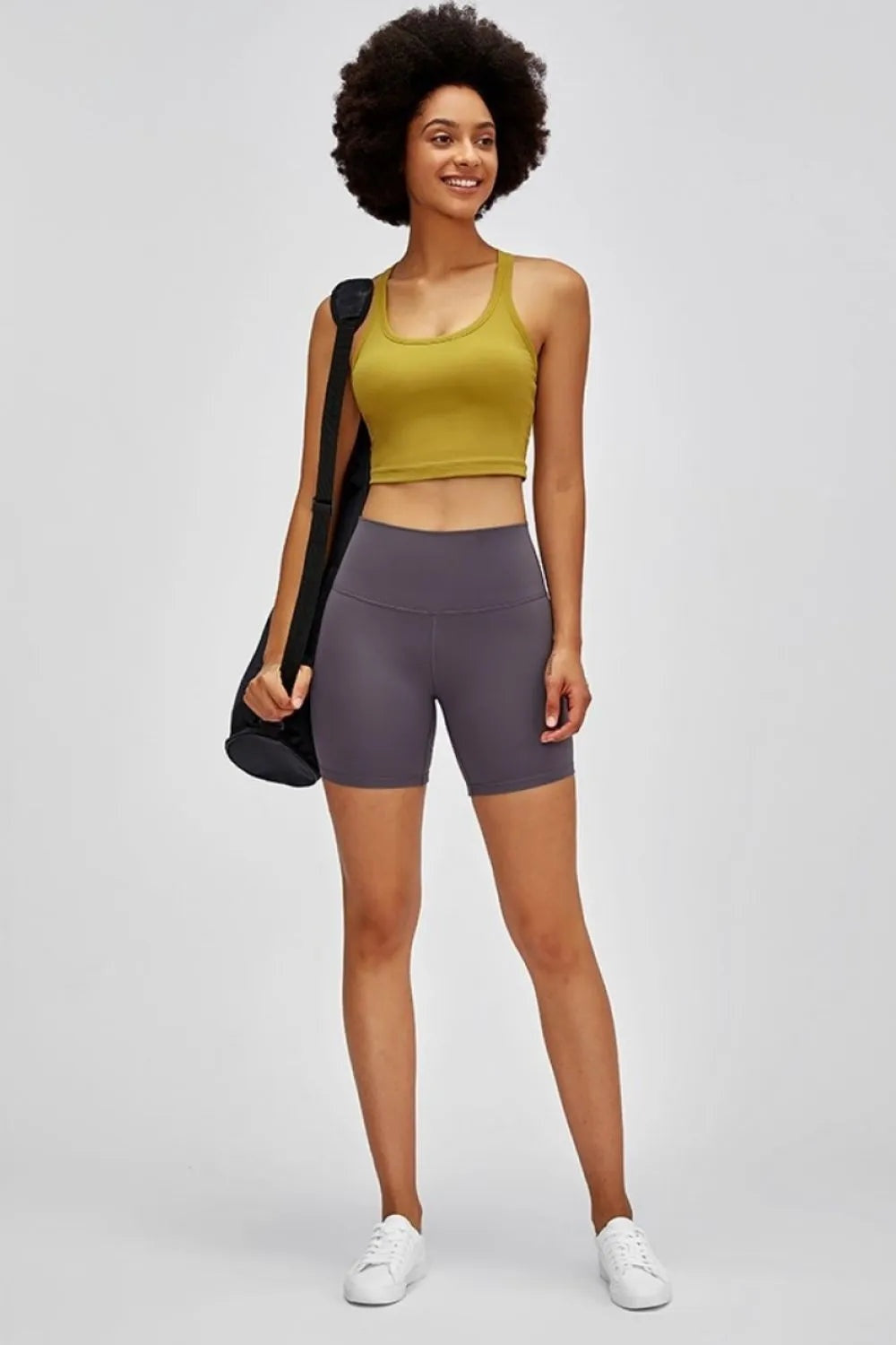 A model stands wearing charcoal gray high-waist training shorts with a wide waistband, stretchy fitted silhouette, and above-knee bike-short length.