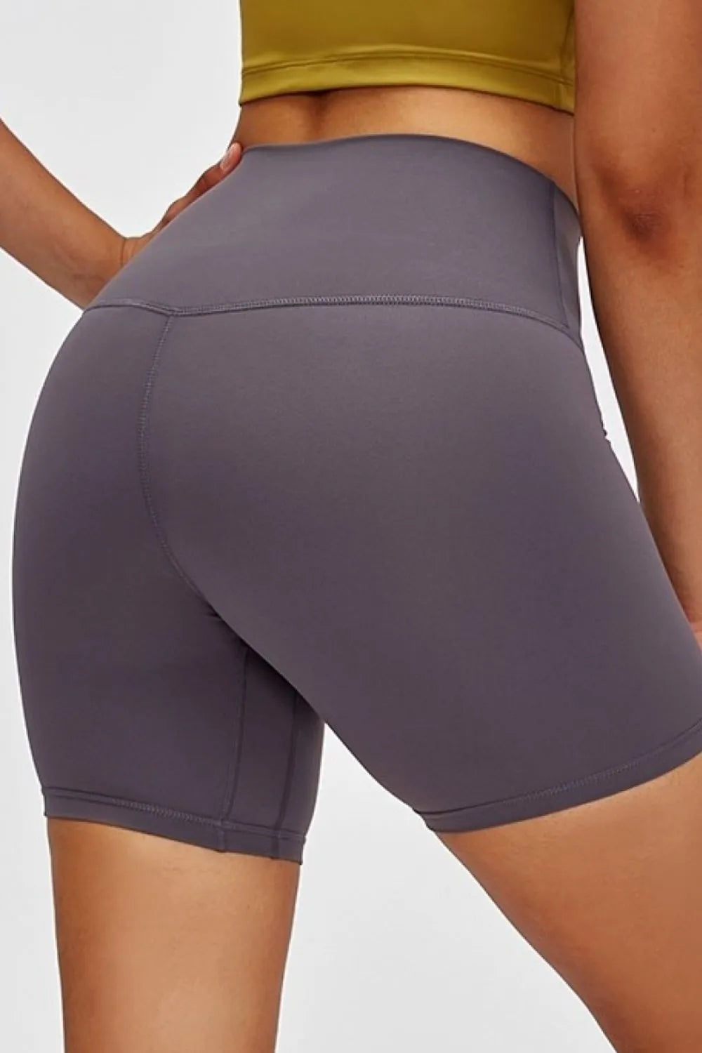 A model poses in dark gray high-waist training shorts with a fitted, stretchy silhouette, mid-thigh length, and visible waistband and seam construction.