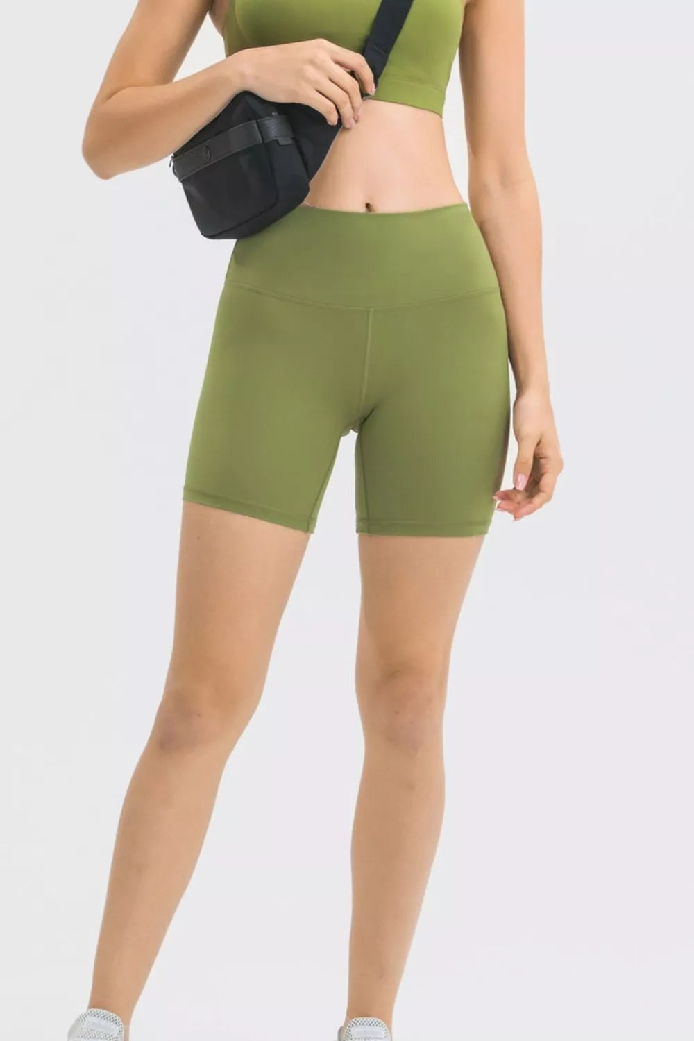 Model wearing olive green high waist training shorts with a fitted stretch silhouette, wide waistband, smooth seams, and mid-thigh length.