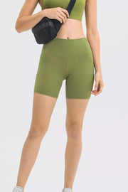 Model wearing olive green high waist training shorts with a fitted stretch silhouette, wide waistband, smooth seams, and mid-thigh length.
