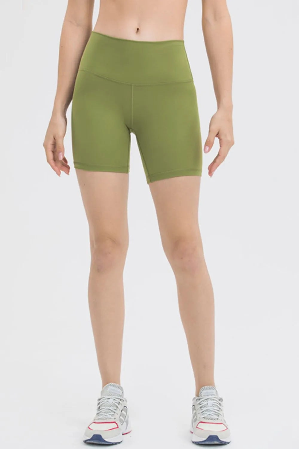 Model stands facing forward in olive green high-waist training shorts with a smooth fitted silhouette, stretch construction, wide waistband, and mid-thigh length.