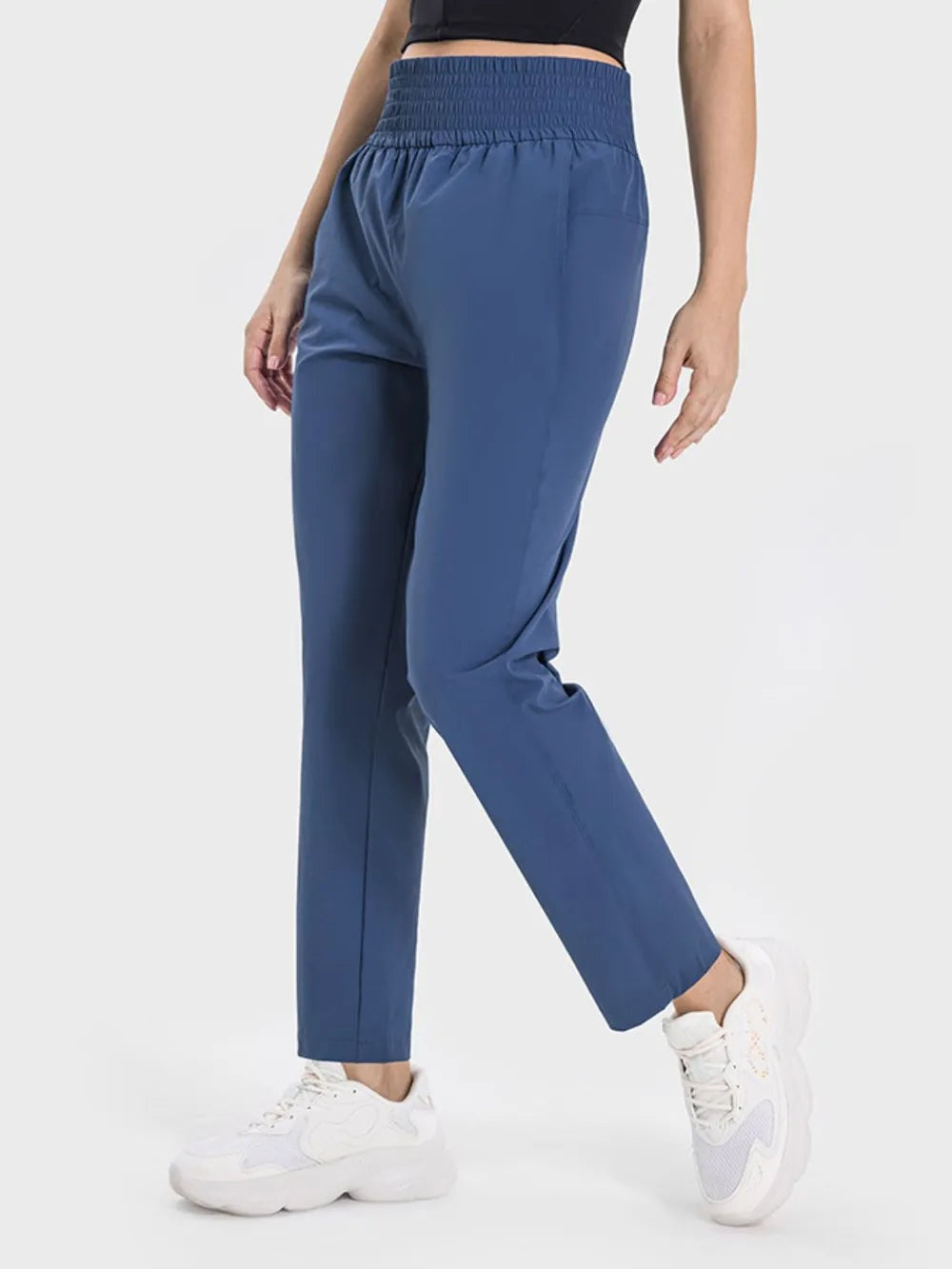 Model poses in blue pocketed high waist active pants with a wide elastic waistband, relaxed straight-leg silhouette, and moderate stretch.