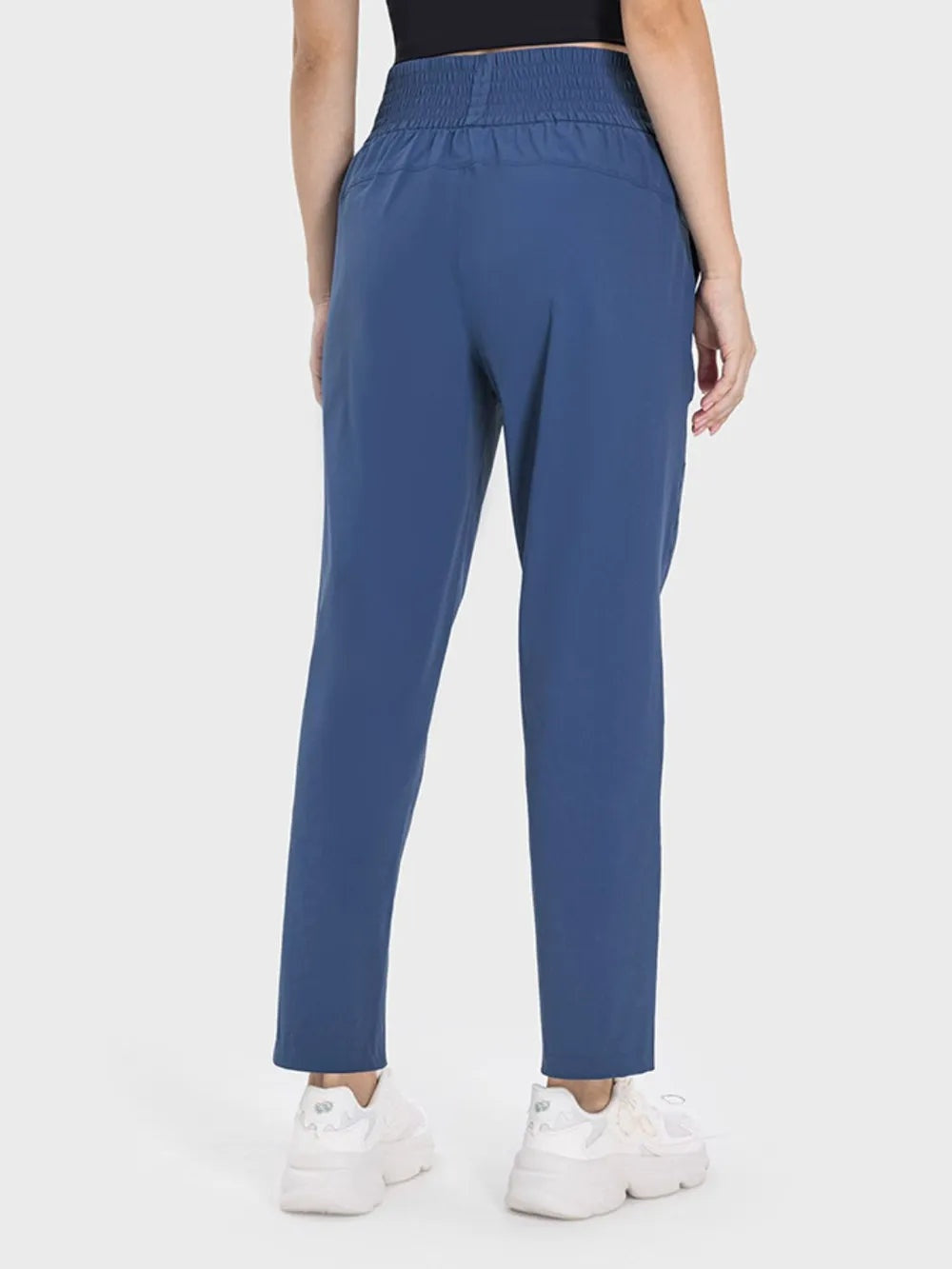 Model shown from behind wearing blue high-waist active pants with an elastic waistband, relaxed straight-leg silhouette, and visible side pockets.