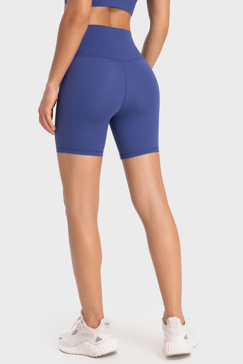 Model shown from behind wearing solid blue sporty biker shorts with a wide waistband, fitted silhouette, mid-thigh length, and visible seam construction.