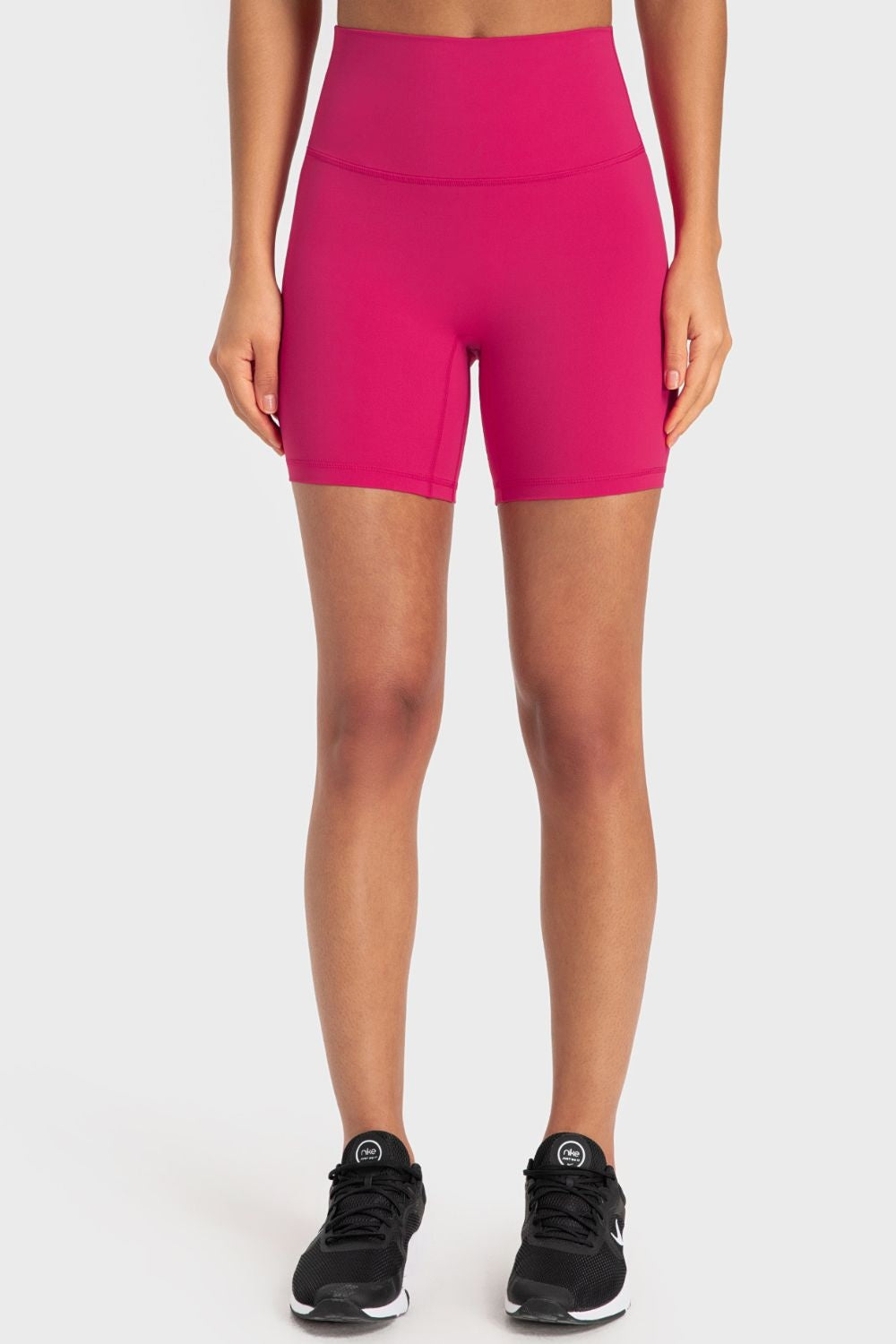 Model wearing solid hot pink wide-waistband biker shorts with a fitted, mid-thigh silhouette and visible front seam construction.