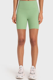Model stands facing forward in solid mint green wide-waistband biker shorts with a fitted mid-thigh silhouette and visible curved seam construction.