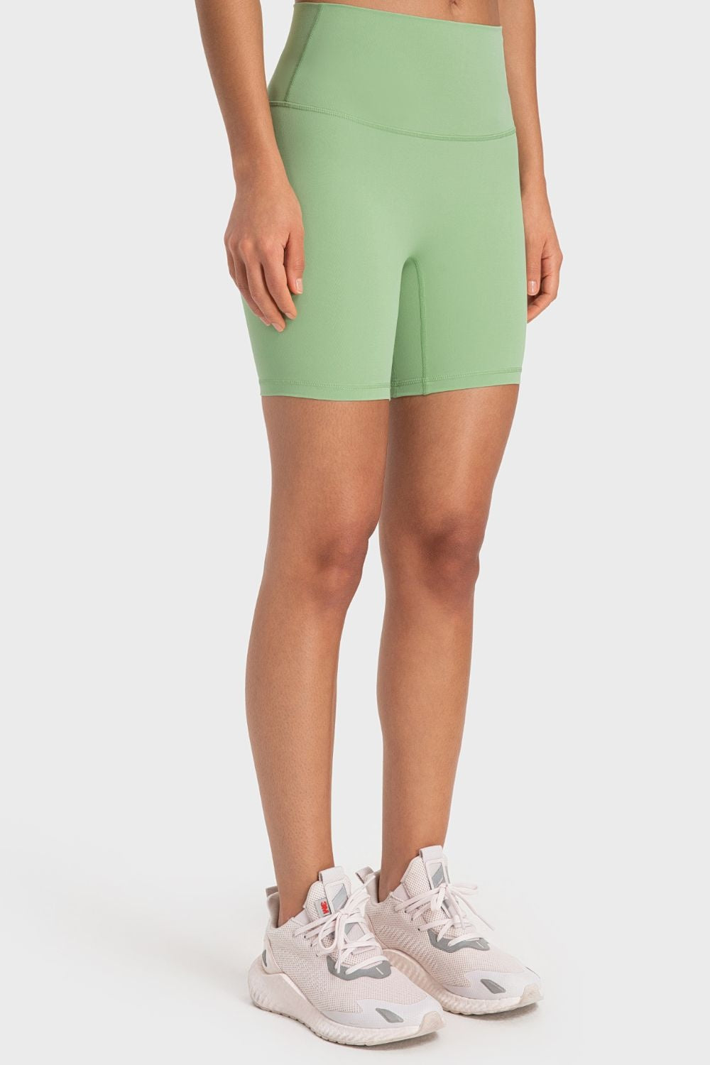 Model wears solid sage green sporty biker shorts with a wide high-rise waistband, fitted silhouette, and visible front seam construction.