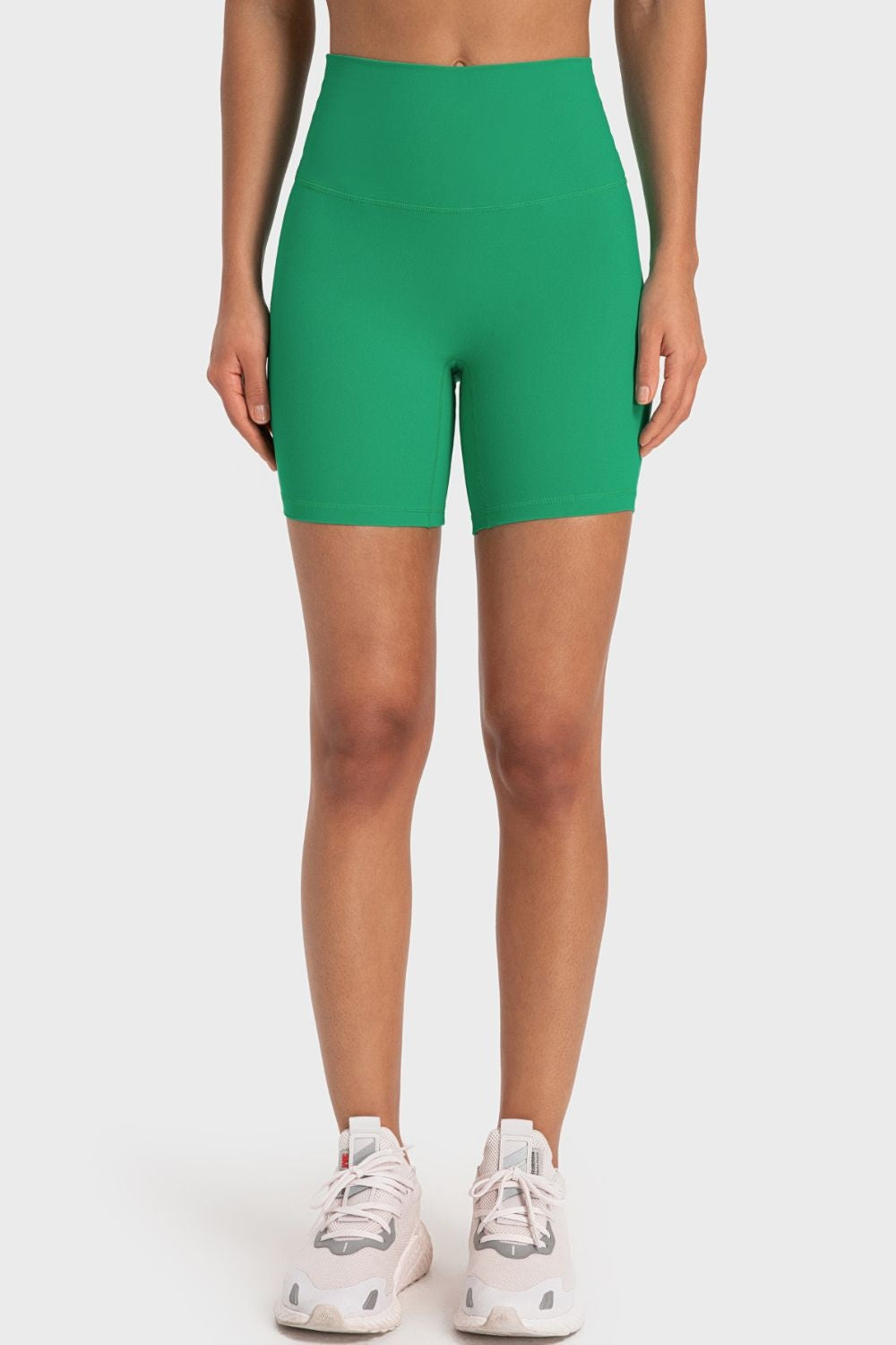 Model standing in bright green solid biker shorts with a wide waistband, fitted mid-thigh silhouette, and clean seamed construction.