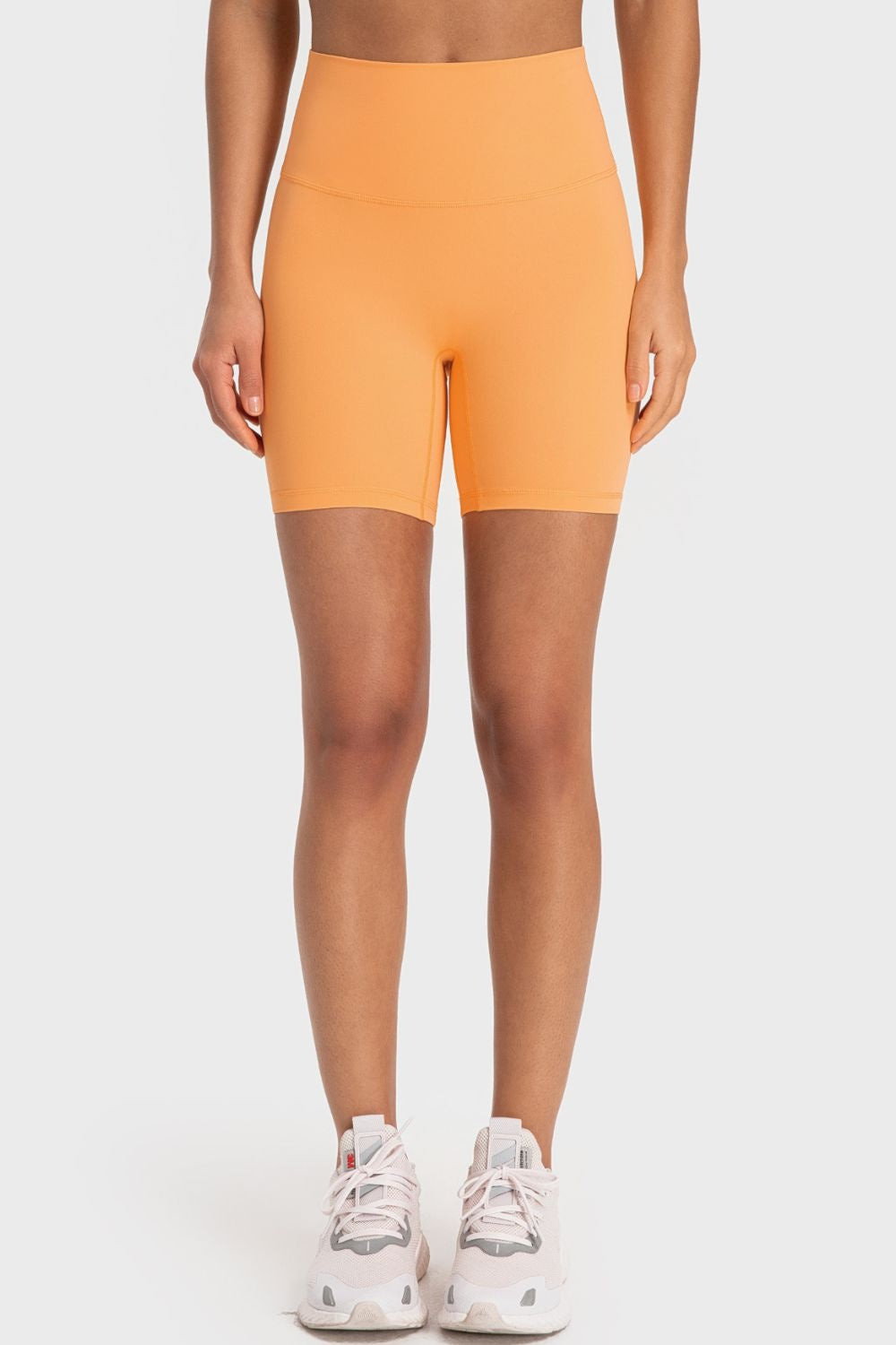 Model wearing solid orange wide-waistband biker shorts with a fitted, mid-thigh silhouette and visible waistband seam.
