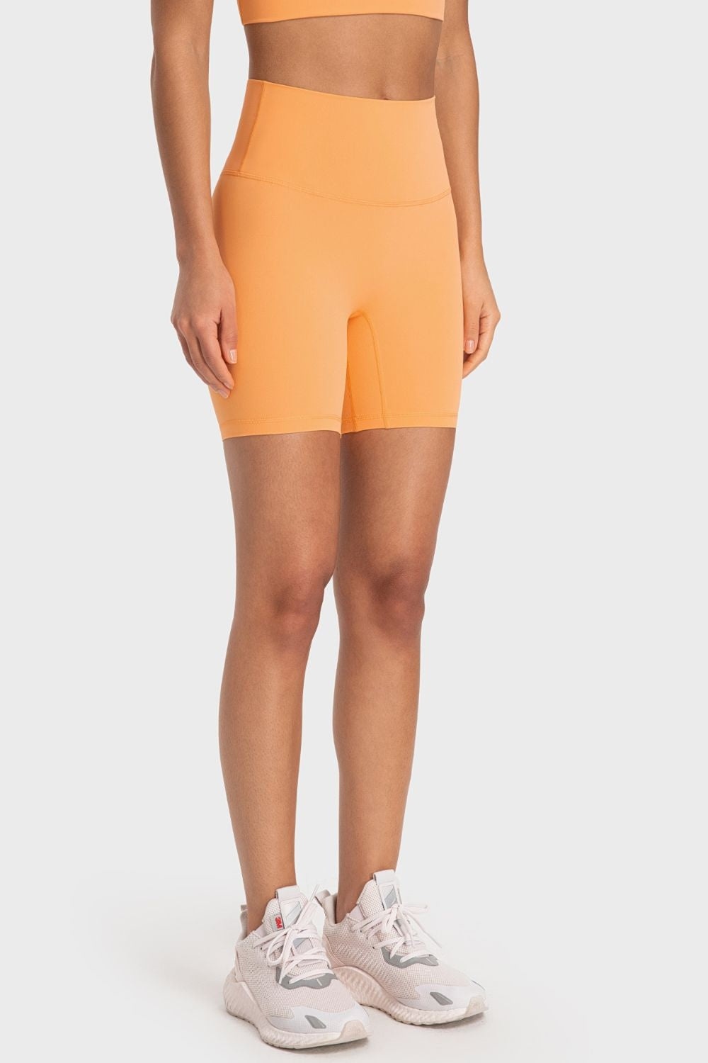 Model standing in bright orange solid biker shorts with a wide waistband, fitted mid-thigh silhouette, and clean seamed construction.