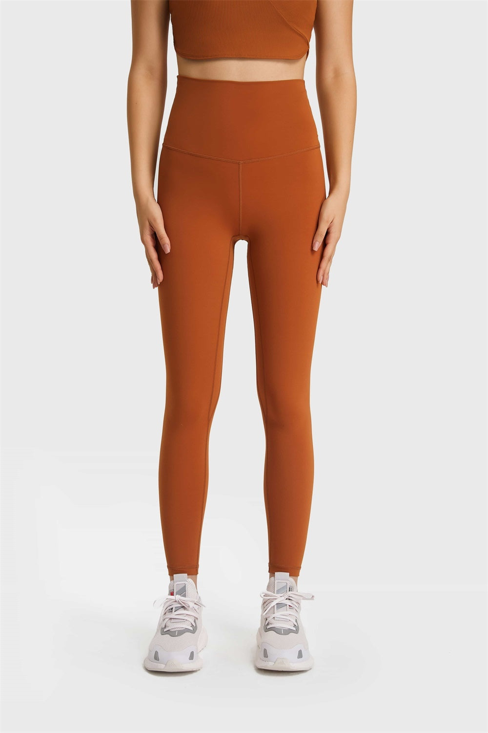 Model standing in rust-orange Ultra Soft High Waist Leggings with a smooth, stretchy fitted silhouette, wide elastic waistband, and long tapered legs.